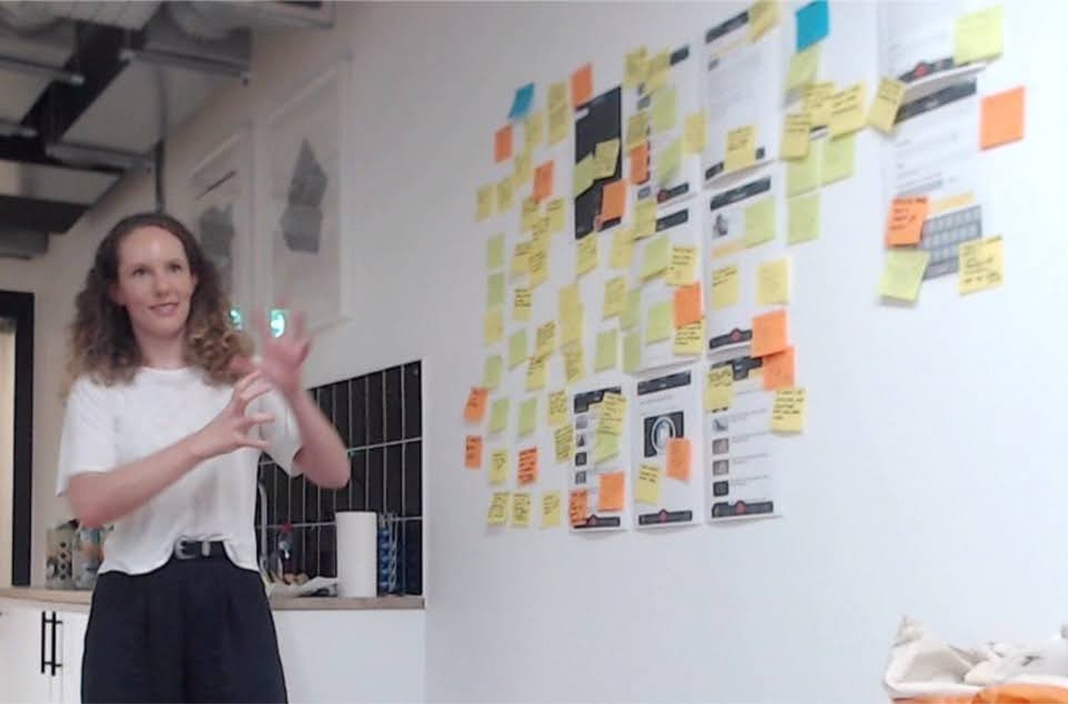In-person research session with a contributor presenting findings on a wall of sticky notes and printed screenshots
